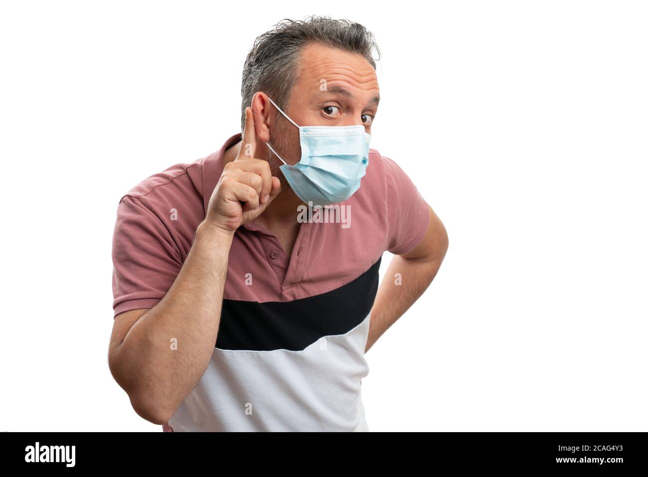 Listening gesture made by curious adult man touching ear with index finger wearing disposable protective cover mask in pandemic isolated on white back Stock Photo