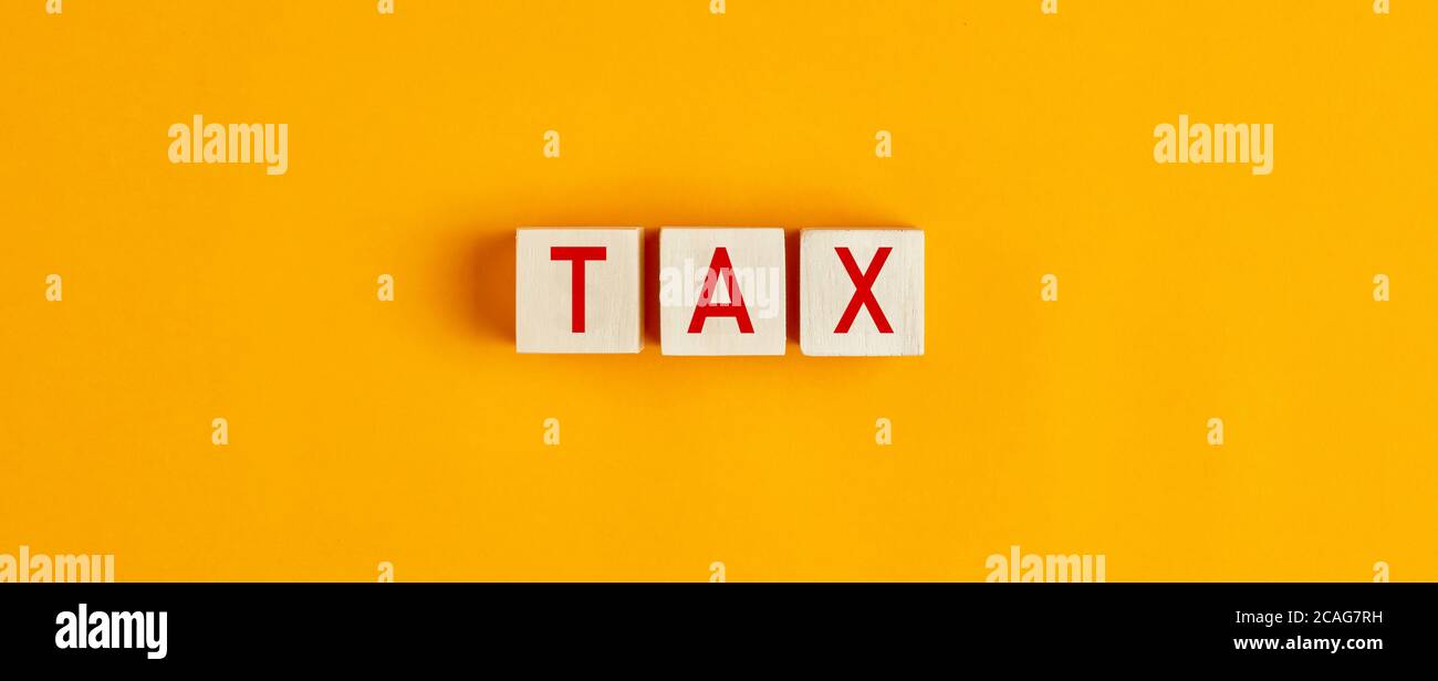 The word tax on wooden blocks against yellow background. Stock Photo