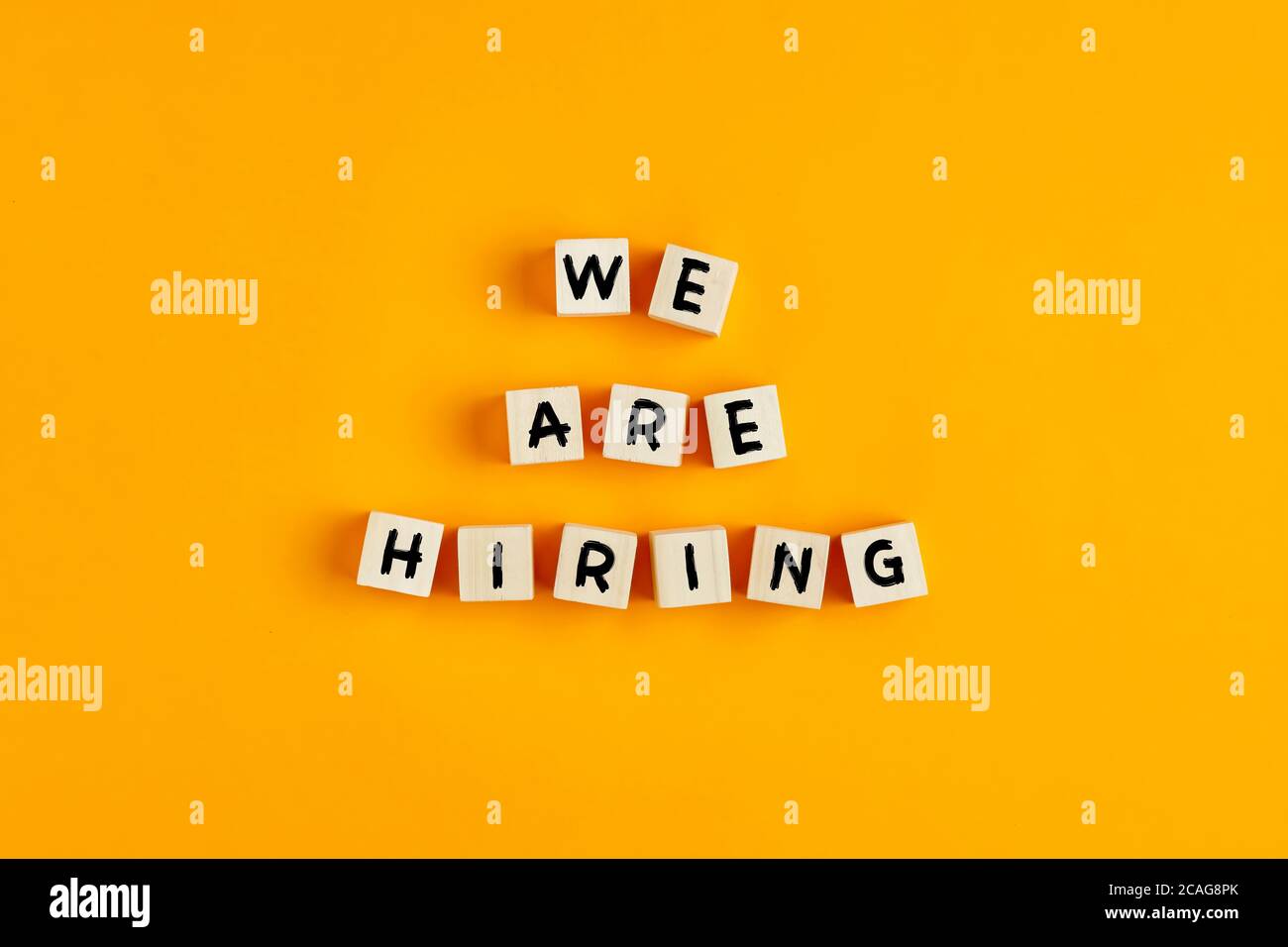 We are hiring text on wooden blocks against yellow background. Concept of human resources recruitment, employment or hire for a job. Stock Photo