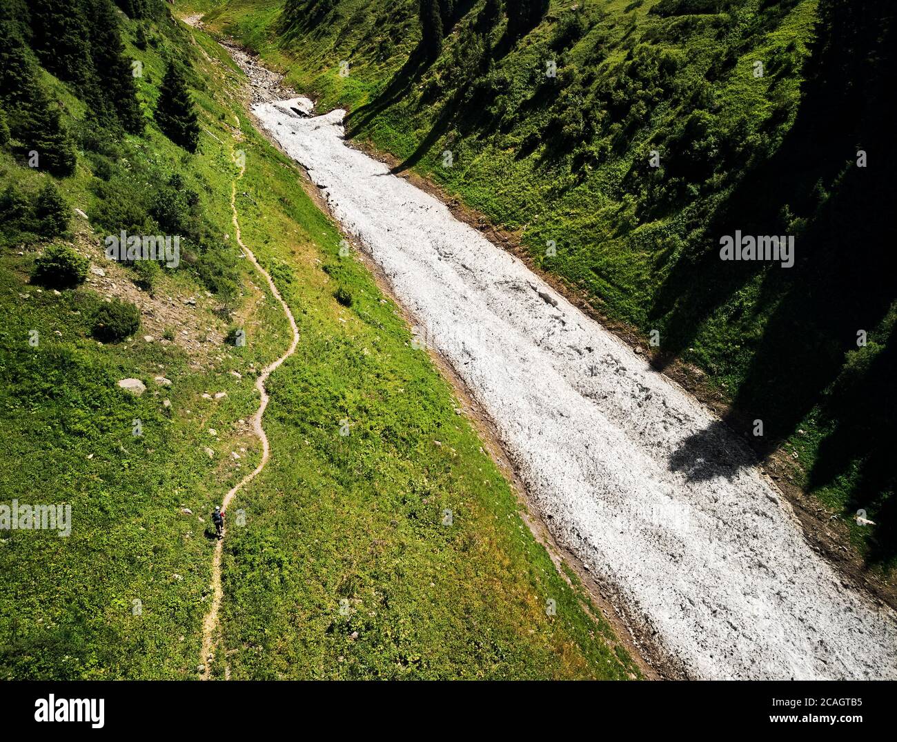 Small man walking near snow glacier in the green mountain valley. Aerial view picture taken by drone. Stock Photo