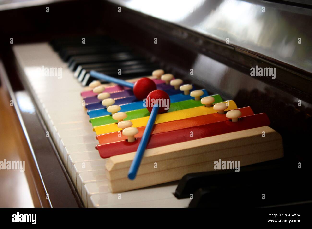 Close up image of a colorful toy xylophone with mallets put on the keyboard of a classical piano. Stock Photo