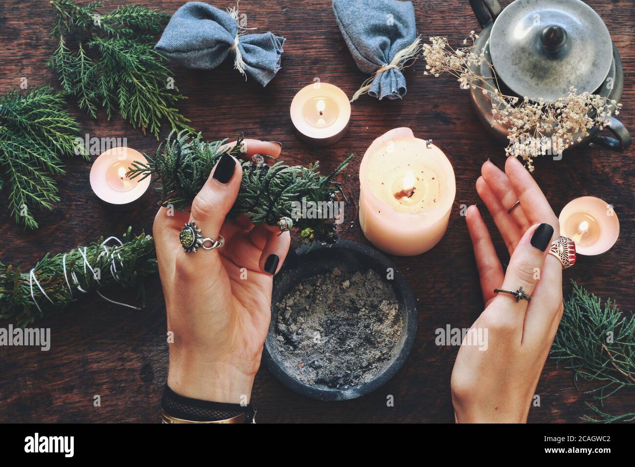 Wiccan witch holding cedar cleansing stick to cleanse the energy at her altar. Female woman holding evergreen smoke cleansing stick in her hands Stock Photo