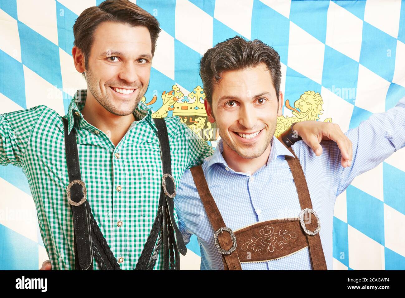 Two smiling men in lederhosen with the Bavarian flag celebrate the Oktoberfest Stock Photo