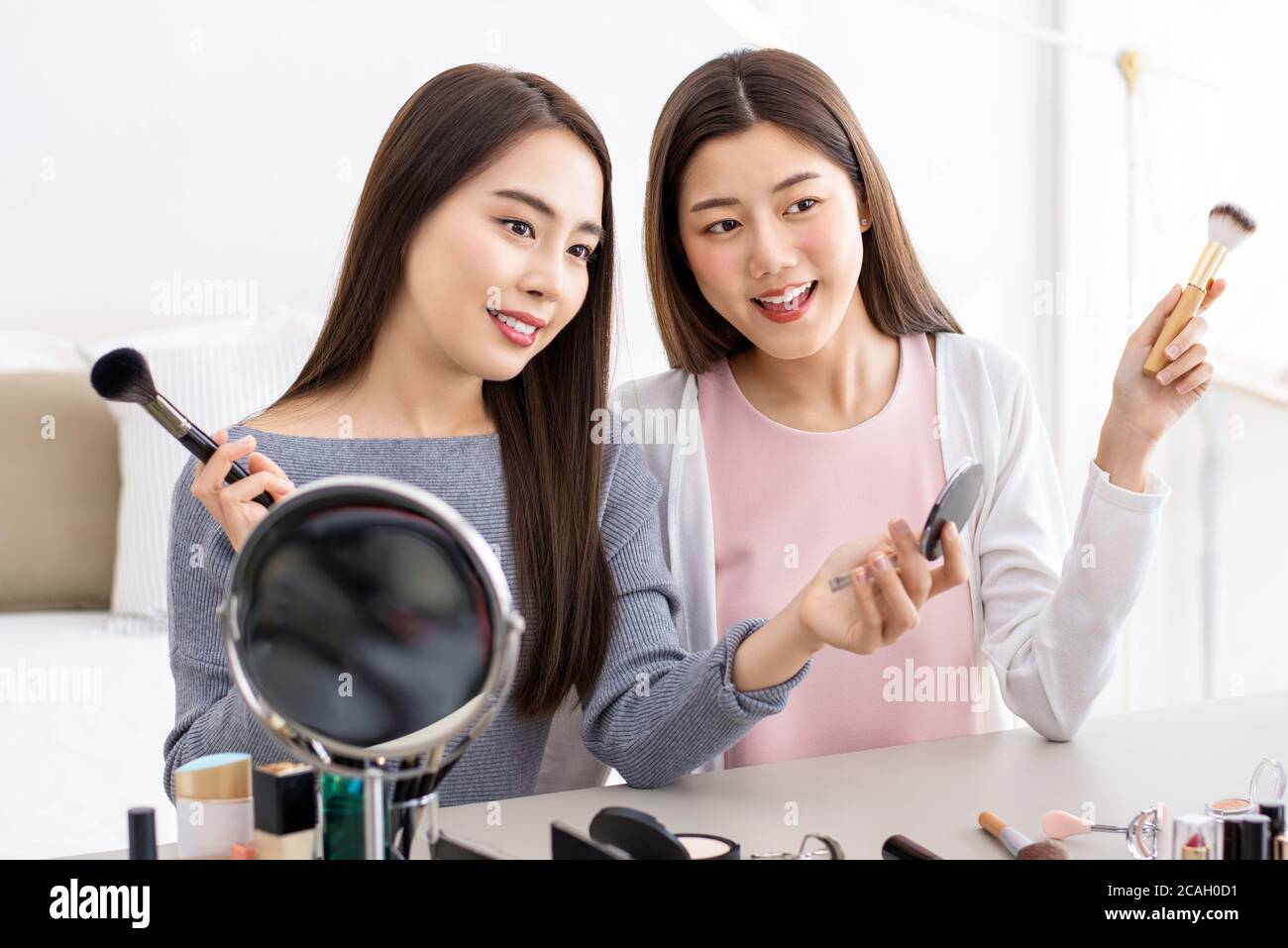 Two pretty Asian beauty influencer girl friends greeting audiences while making live recording at home Stock Photo