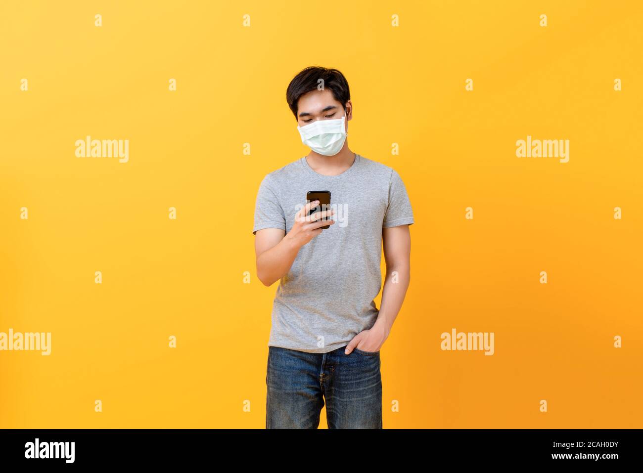 Young Asian man wearing medical face mask using mobile phone isolated ...