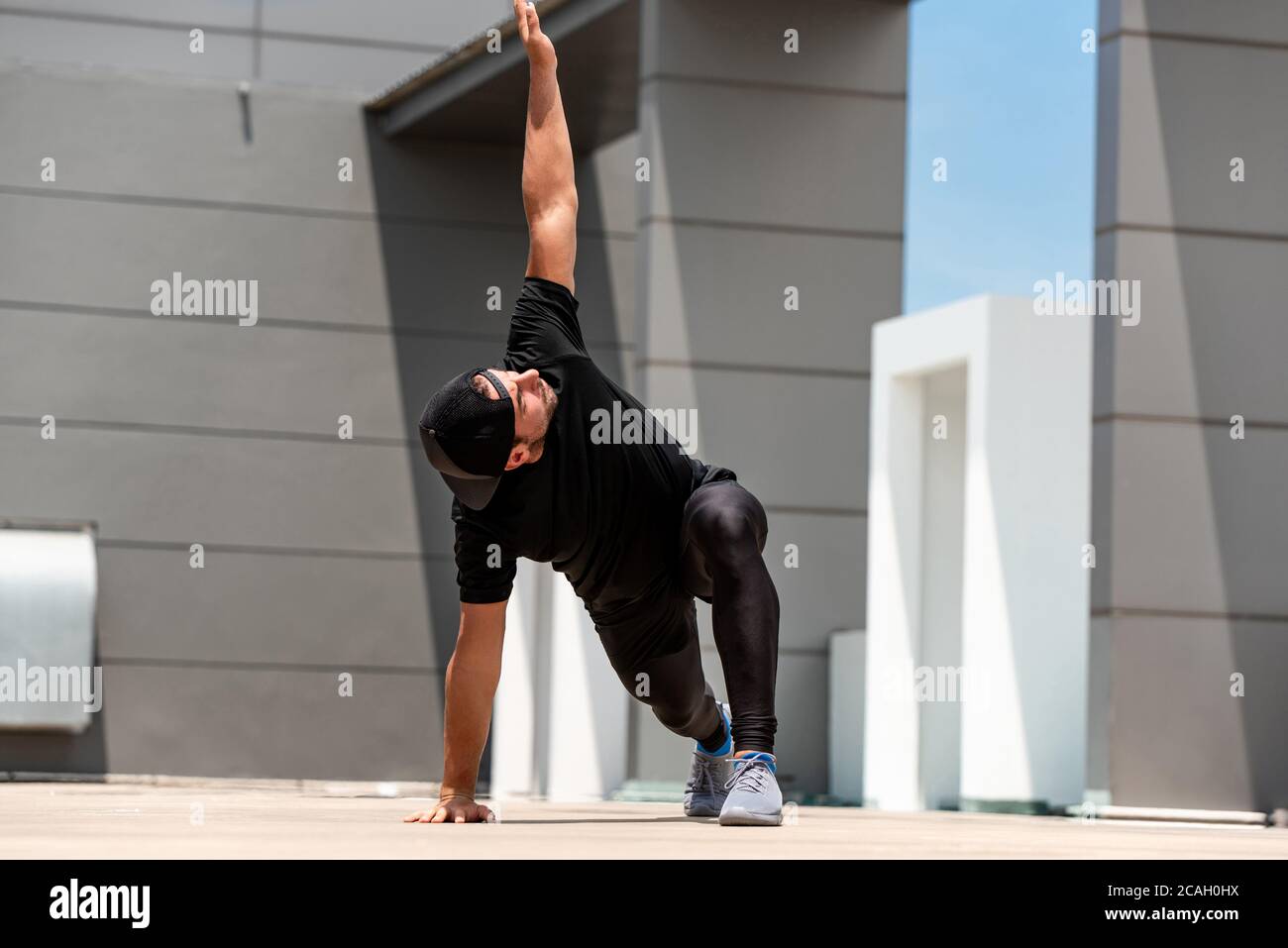 Fit sports man warming up with spider lunge exercise outdoors on building rooftop floor Stock Photo