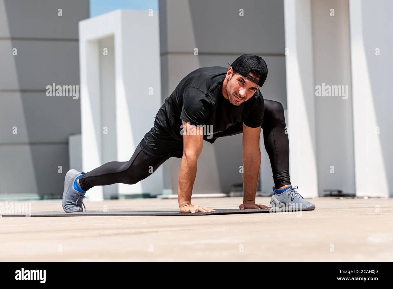 Fit handsome sports man warming up with spider lunge exercise outdoors on building rooftop floor Stock Photo