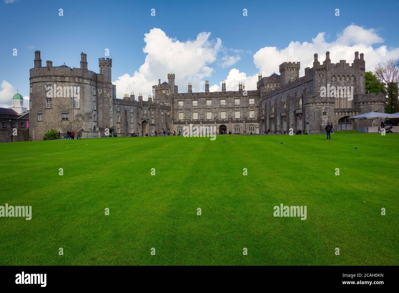 View of the main facade of Kilkenny Castle where several tourists stroll through the park. Kilkenny, Ireland Stock Photo