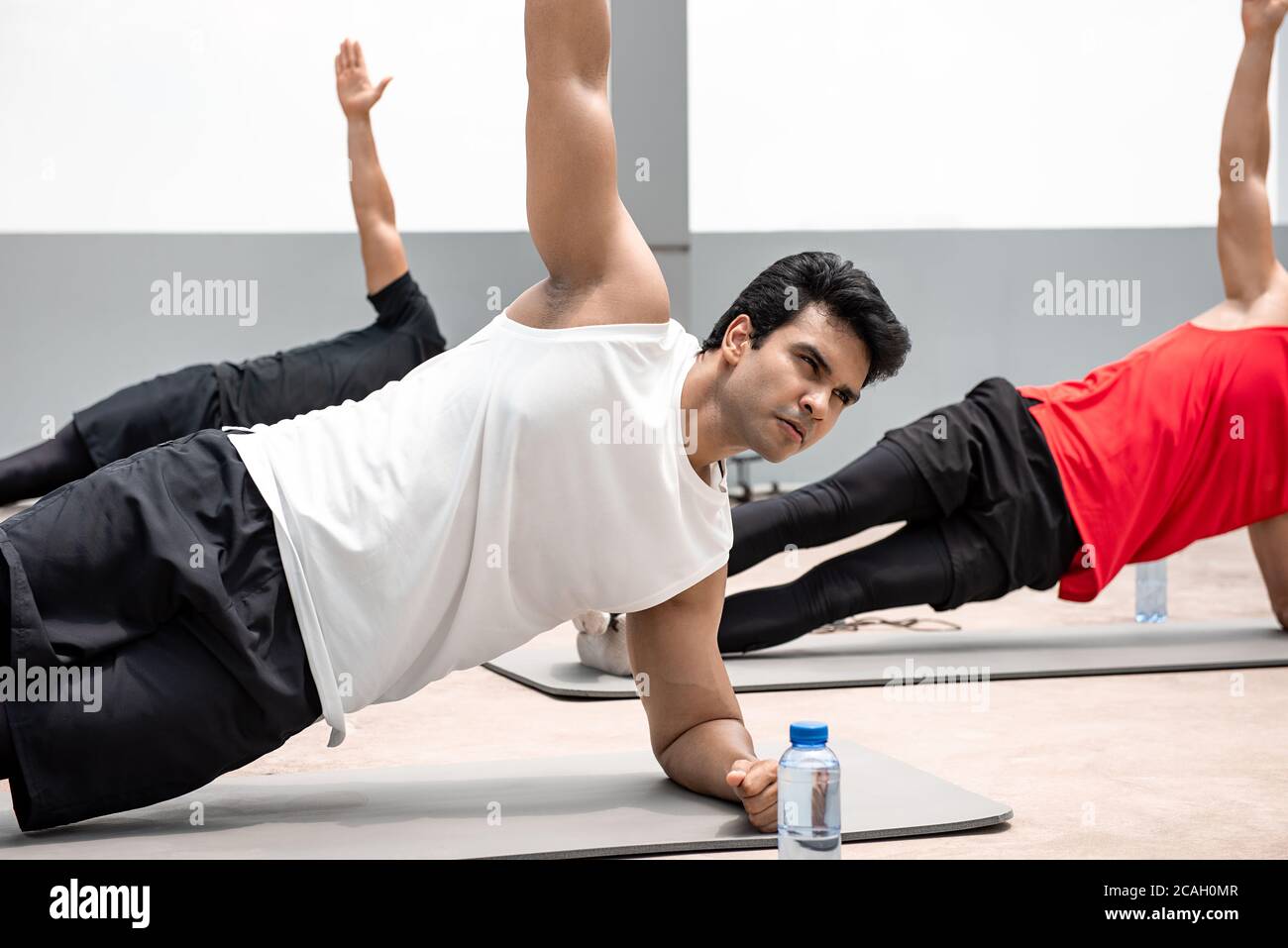 Athletic Indian man doing side plank exercise outdoors on rooftop with friends Stock Photo