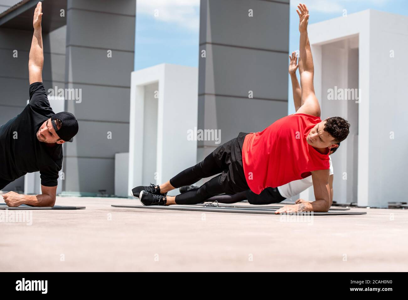 Group of athletic men doing side plank workout exercise outdoors on rooftop floor Stock Photo