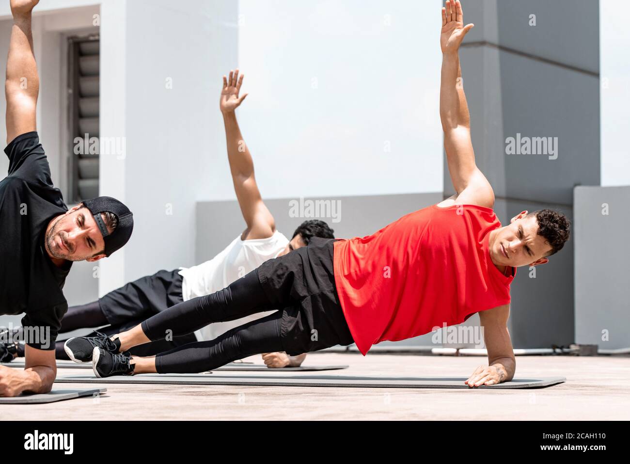 Handsome athletic men doing side plank bodyweight workout training outdoors on building rooftop in sunlight Stock Photo
