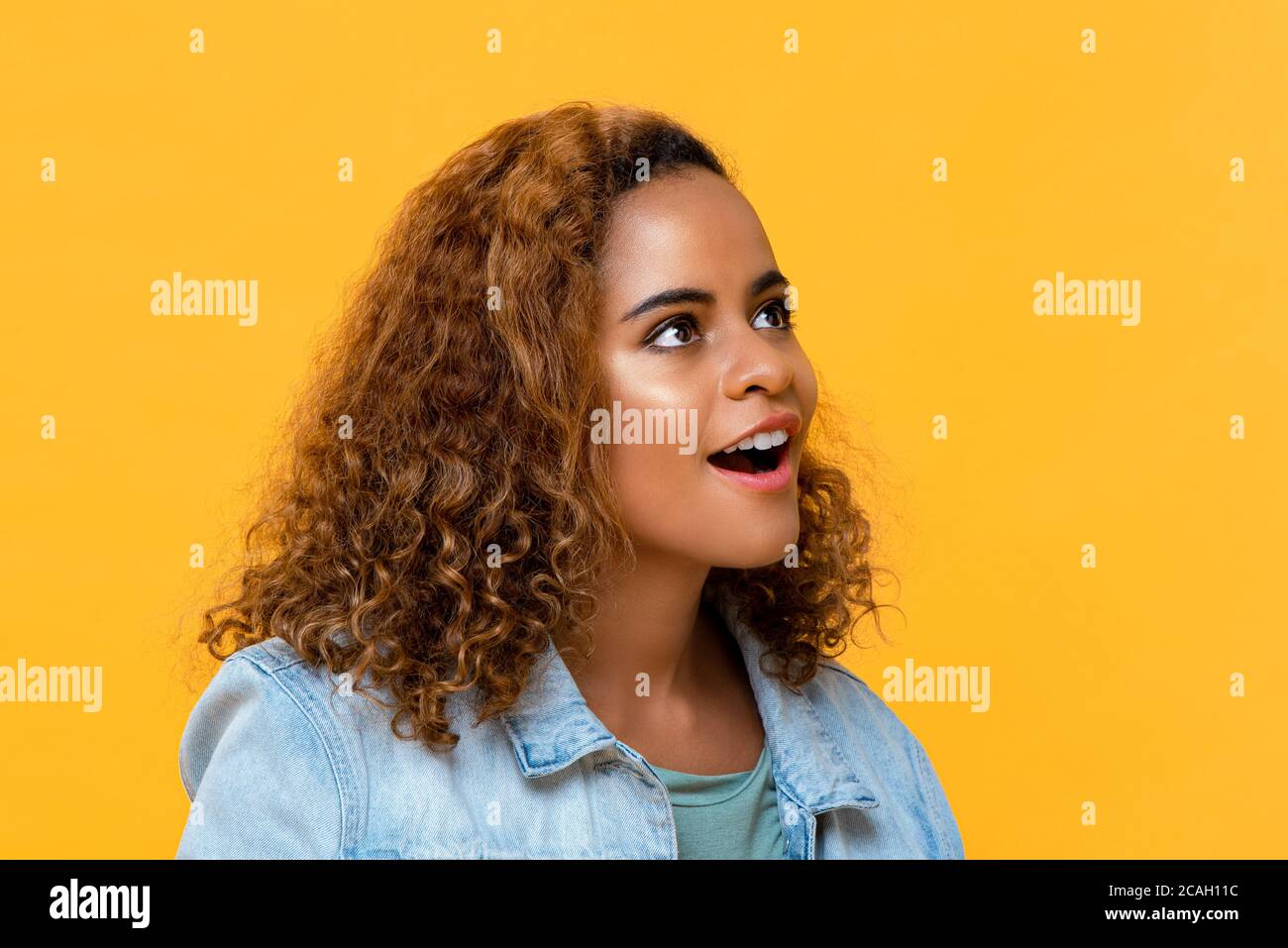 Close up portrait of surprising young beautiful African American woman looking up in isolated studio yellow background Stock Photo