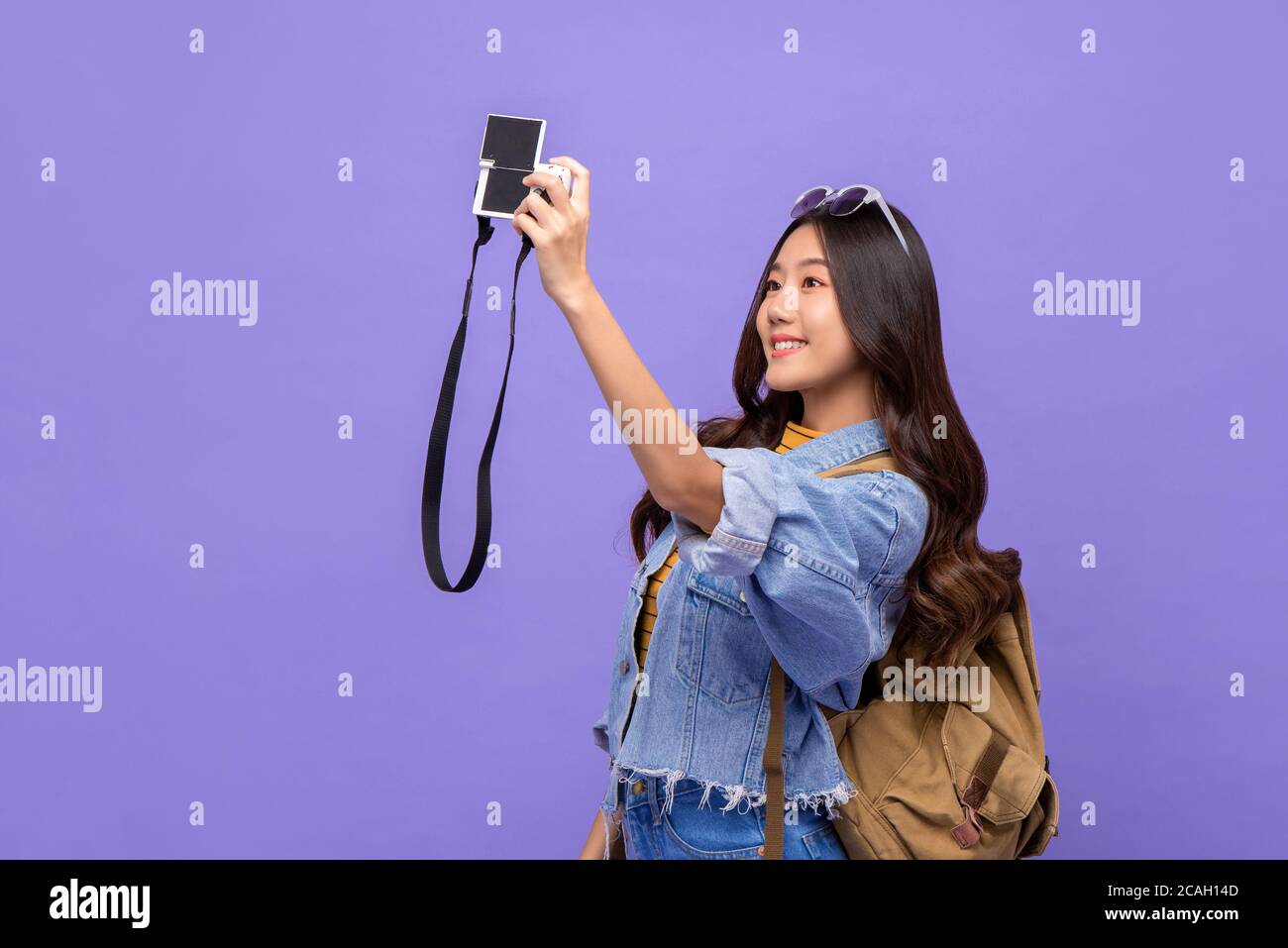Smiling young Asian woman tourist backpacker taking selfie with camera isolated on purple background Stock Photo