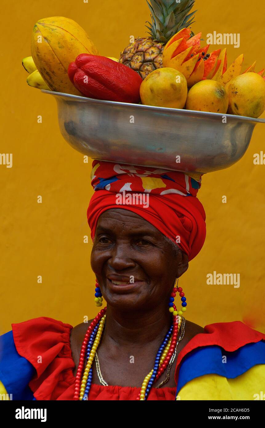Lady in colorful traditional attire posing while carrying a fruit