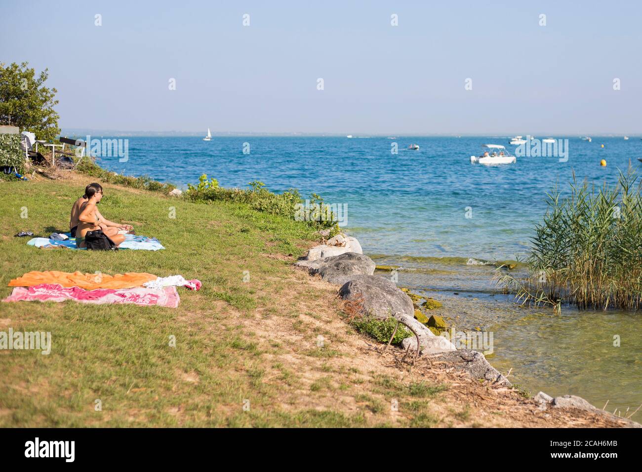 People chilling on the grass in San Biagio Island, manerba del Garda, Lombardy, Italy. Stock Photo