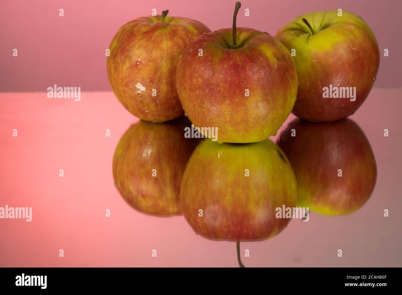 Three red apples on mirroring table on mirror red background with reflection isolated close up Stock Photo