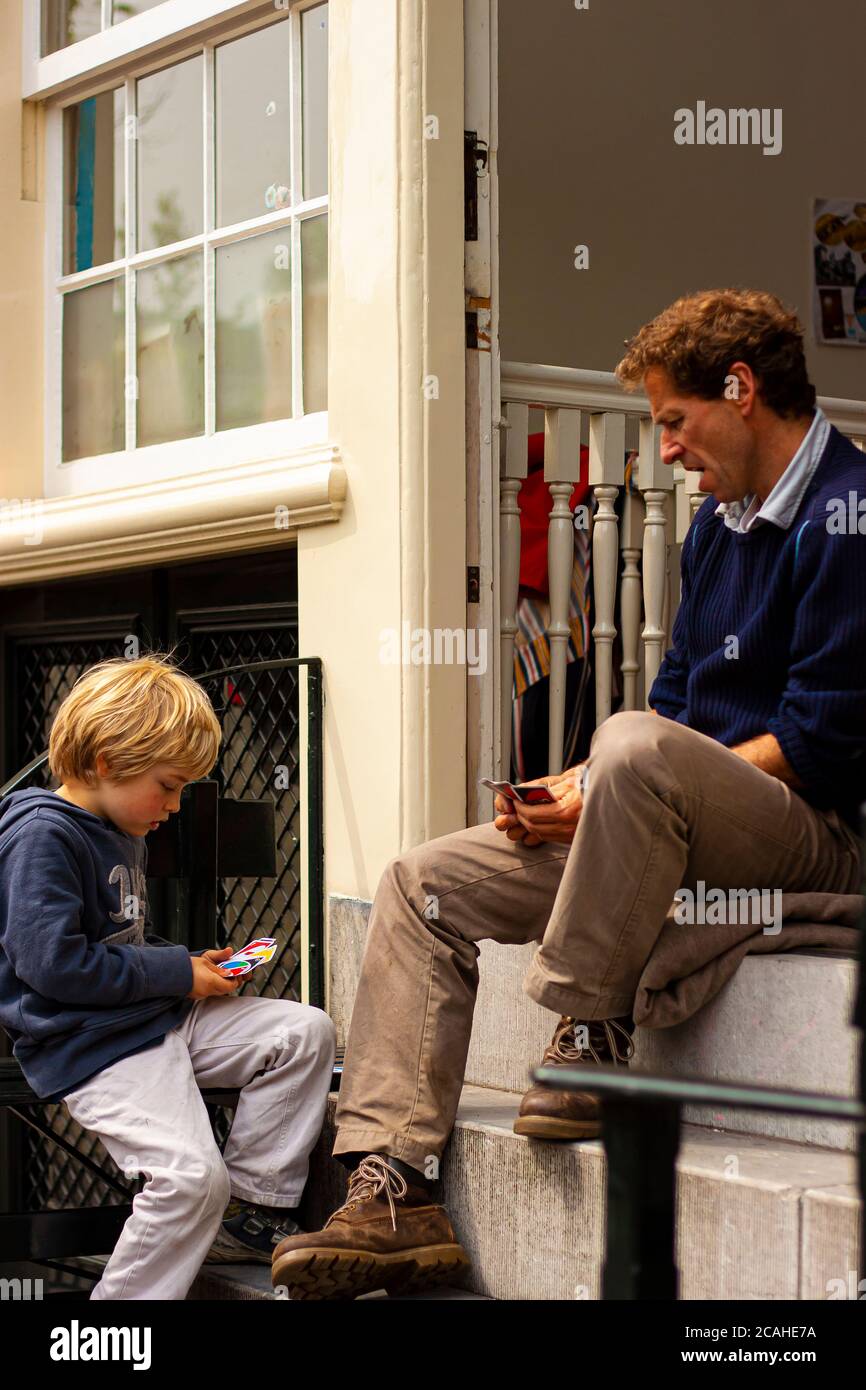 Amsterdam, Netherlands 05/15/2015: A blond boy is sitting on the concrete stairs in front of his home with his father and they are playing a card game Stock Photo