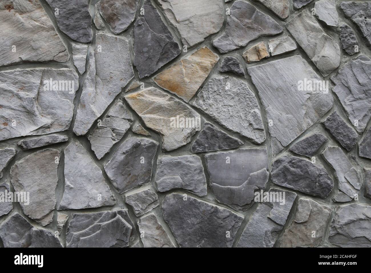 old odd shaped grey black thick cut stone block wall with gray grout shadows straight lines suitable for website background marketing backgrounds back Stock Photo