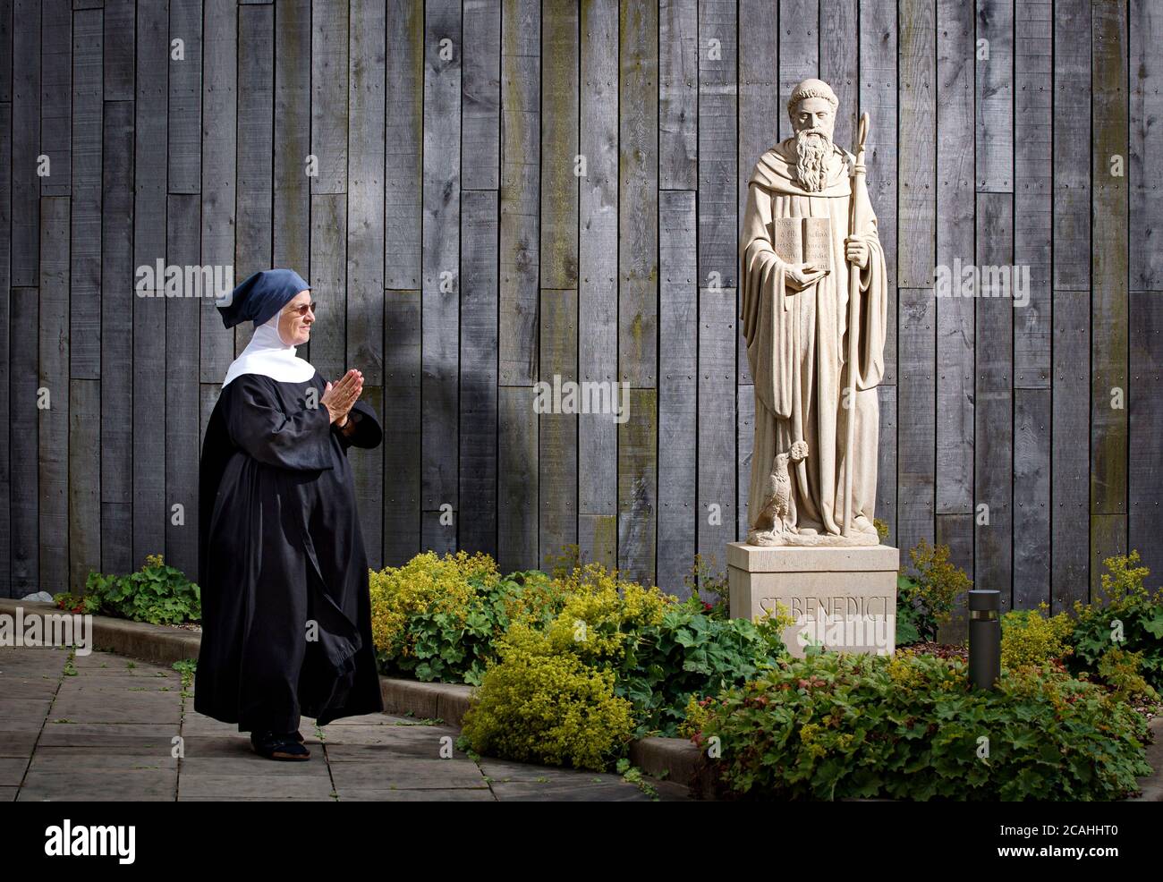 Sister Agnes walks past a newly installed statue of St Benedict at Stanbrook Abbey nunnery in Wass, North Yorkshire. The statue, made by Matthias Garn Master Mason and Partner from a single piece of West Yorkshire fine-grained sandstone, is a replica of an existing statue which became badly weathered due to the harsh climate at Stanbrook Abbey. Stock Photo