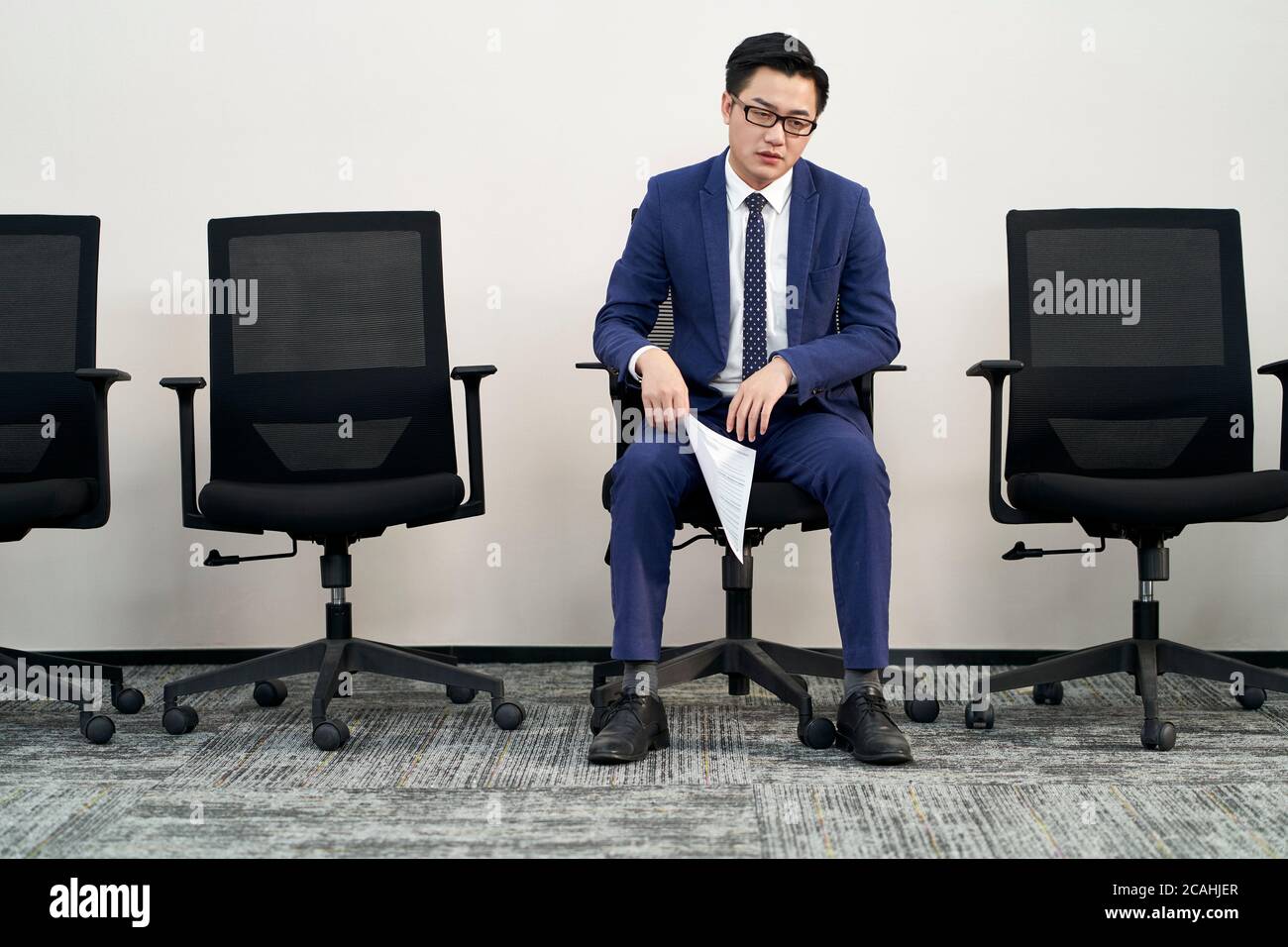 young male asian job seeker sitting in chair appears to be frustrated and defeated Stock Photo