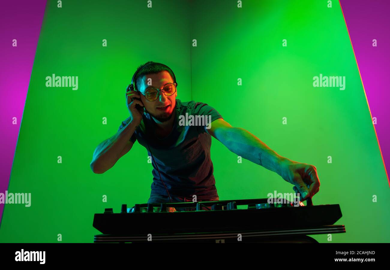 Art. Young caucasian musician in headphones performing on bicolored pink-purple background in neon light. Concept of music, hobby, festival. Joyful party host, DJ. Colorful portrait of artist. Stock Photo