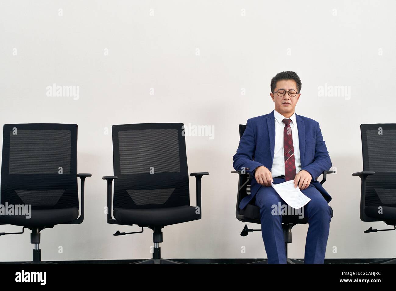 older asian job seeker preparing for interview with eyes closed while waiting in line Stock Photo