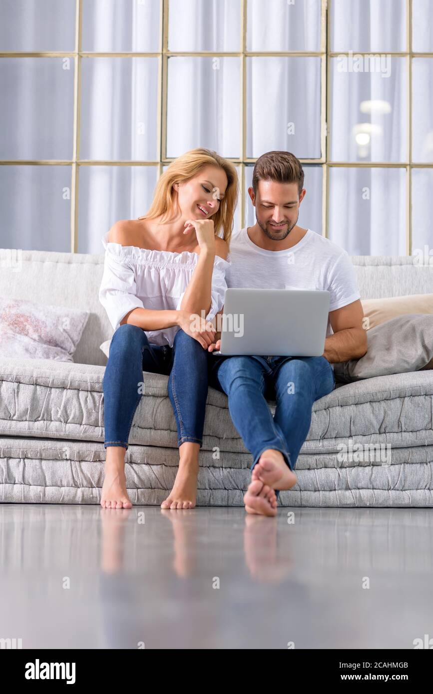 A beautiful young couple sitting on the sofa and using a laptop Stock ...