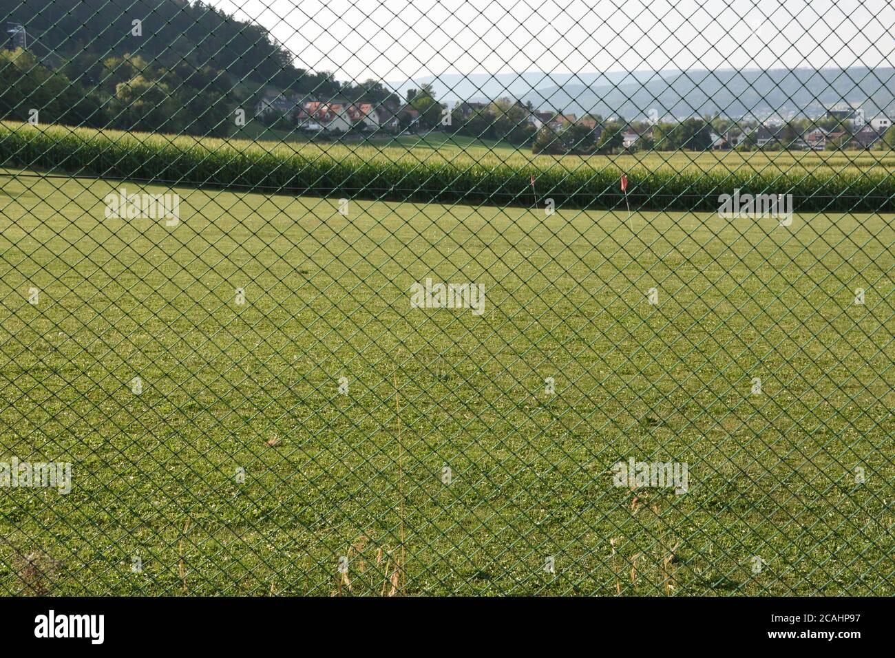 Golf course behind green mesh which form fence with houses of the village, forest and cornfield in background during summer in Urdorf, Switzerland. Stock Photo