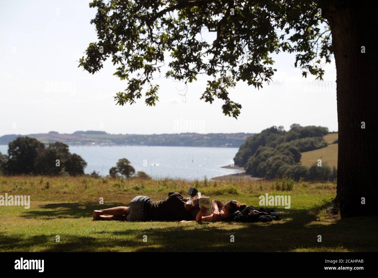 People find shade under a tree at the National Trust's, Trelissick Garden, in Cornwall, as the UK could see record-breaking temperatures with forecasters predicting Friday as the hottest day of the year. Stock Photo