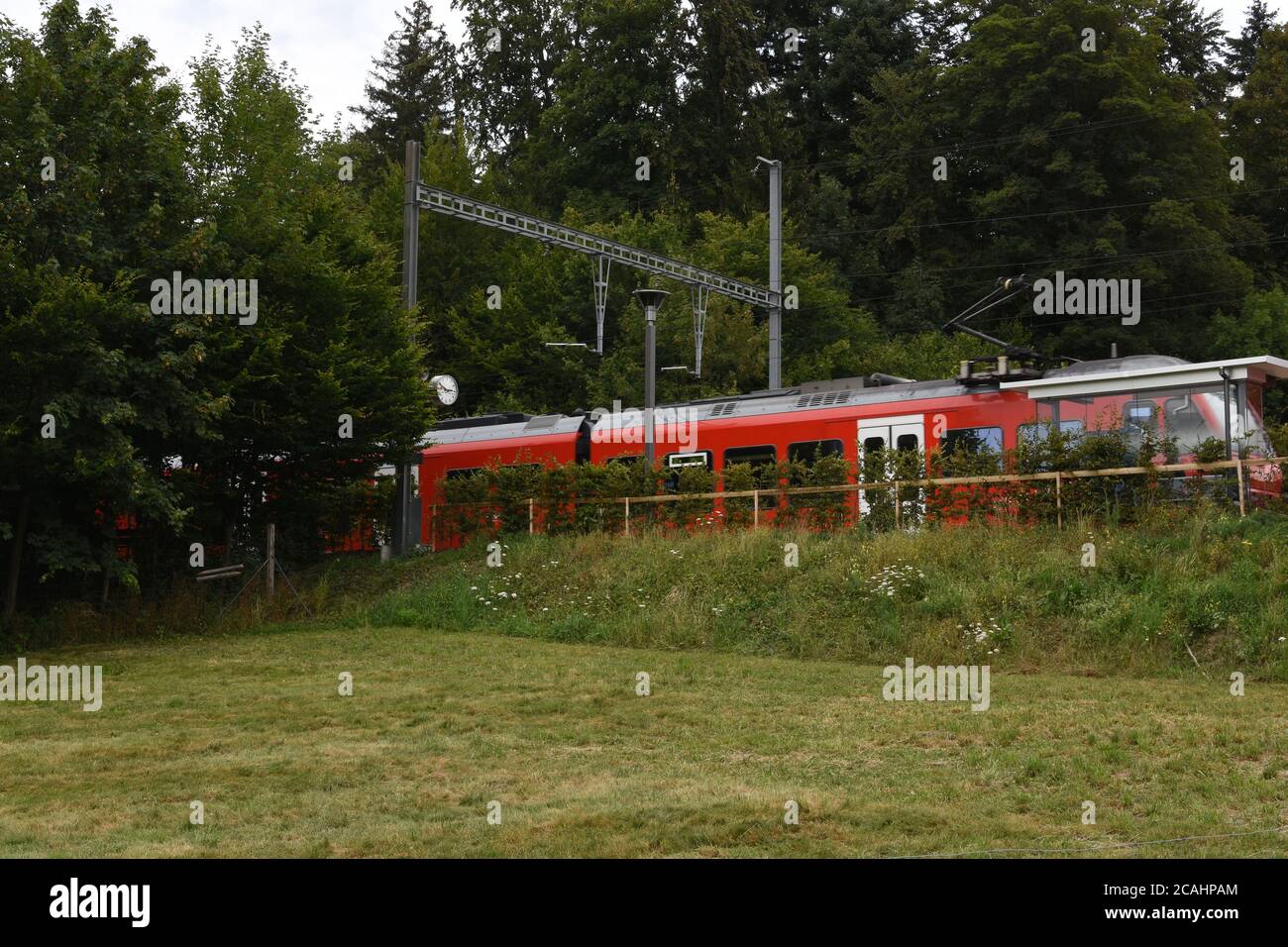 Small railway platform for passengers in local train station in Ringlikon with red electric train heading to Uetliberg mountain in the Swiss plateau. Stock Photo