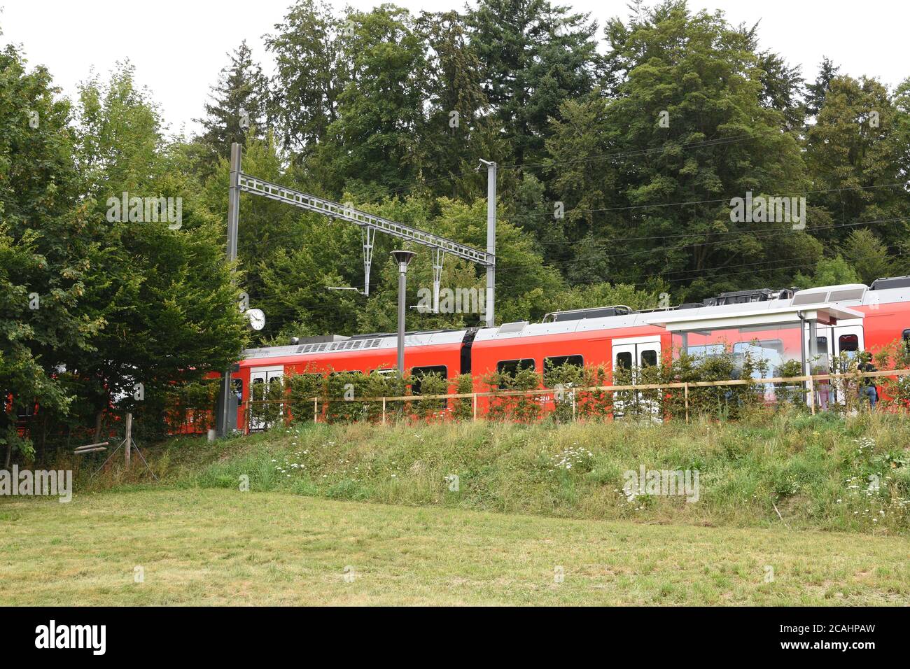 Small railway platform for passengers in local train in Ringlikon station with red train heading to Uetliberg mountain in the Swiss plateau. Stock Photo