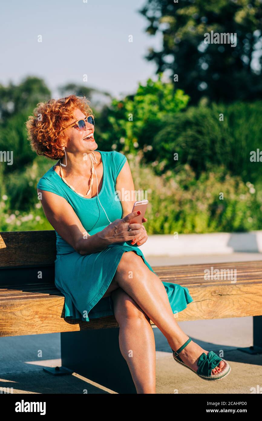Mature woman listening to the music on her smartphone in the park Stock Photo