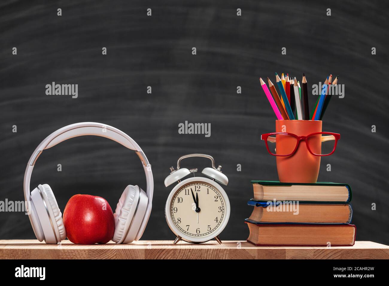 Back to school. Student set. Stack of books pencils glasses alarm clock headphones apple on the background of the black board. Education concept. Stock Photo