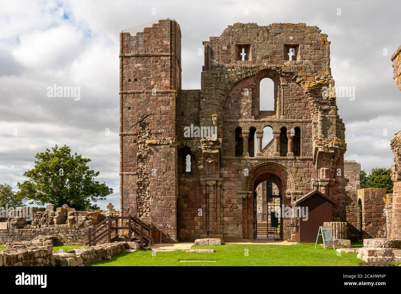 The remains of foundations in the nave of the priory church and the imposing fortified Romanesque style front entrance with its tower and arrow loops Stock Photo