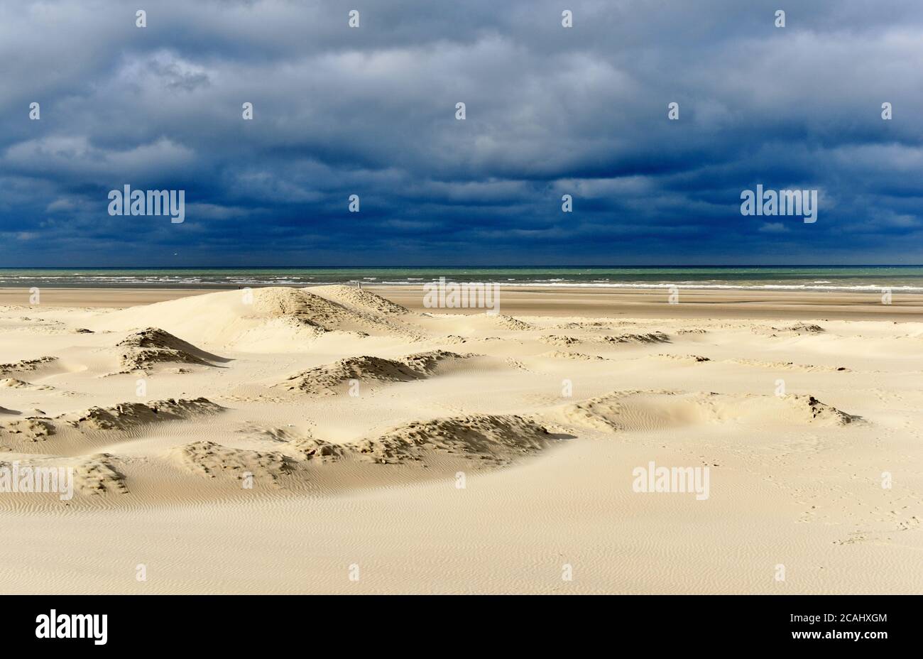 Sunlit sandy dunes under a threatening sky in this autumn beach scene taken in Berck, France. Stock Photo