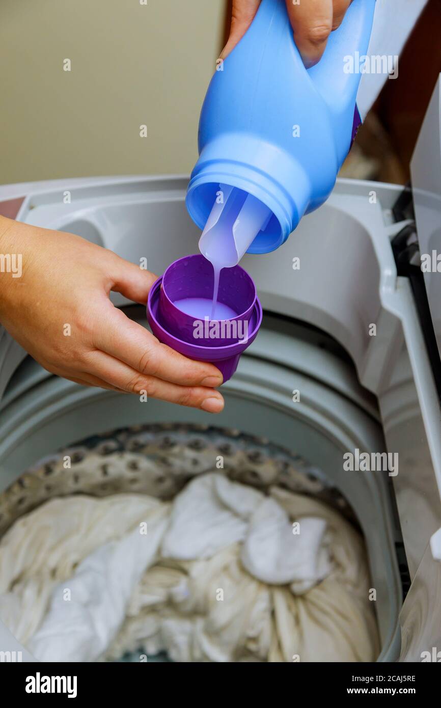 A hand with liquid detergent put into washing laundry machine Stock Photo