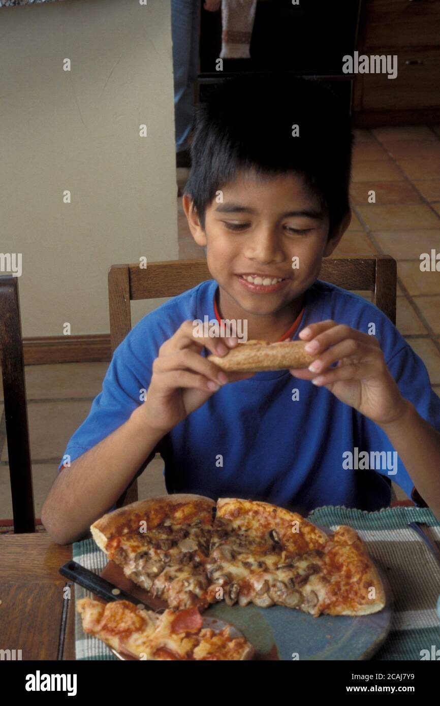 Young Hispanic boy,10 year old, eating pizza at home at dinner table