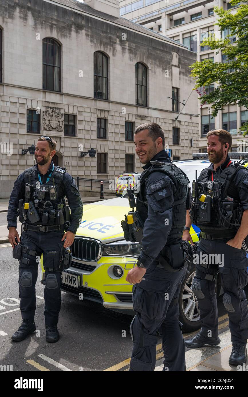 City of London armed police officers take a break and stand in conversation next to parked police car in Wood Street, London, England, UK Stock Photo