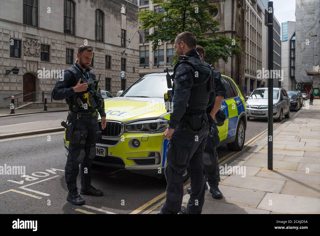 City of London armed police officers take a break and stand in conversation next to parked police car in Wood Street, London, England, UK Stock Photo