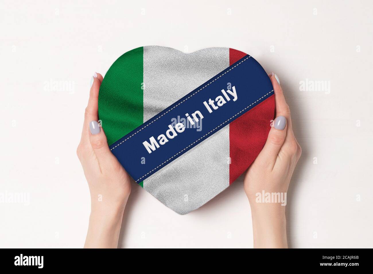Inscription Made in Italy the flag of Italy. Female hands holding a heart shaped box. White background. Stock Photo