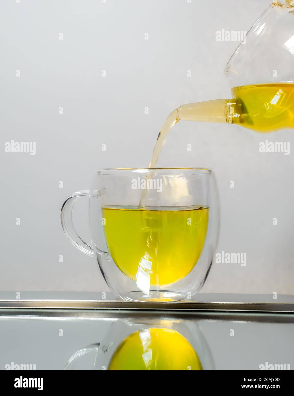 Glass teapot pouring green tea into cup isolated on white Stock Photo