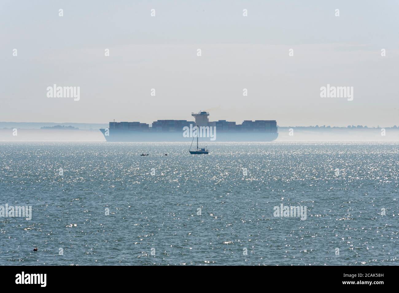 Cargo ship passing a small yacht in the Thames Estuary off Southend on Sea, with a layer of surface mist. River traffic. Sea lanes Stock Photo
