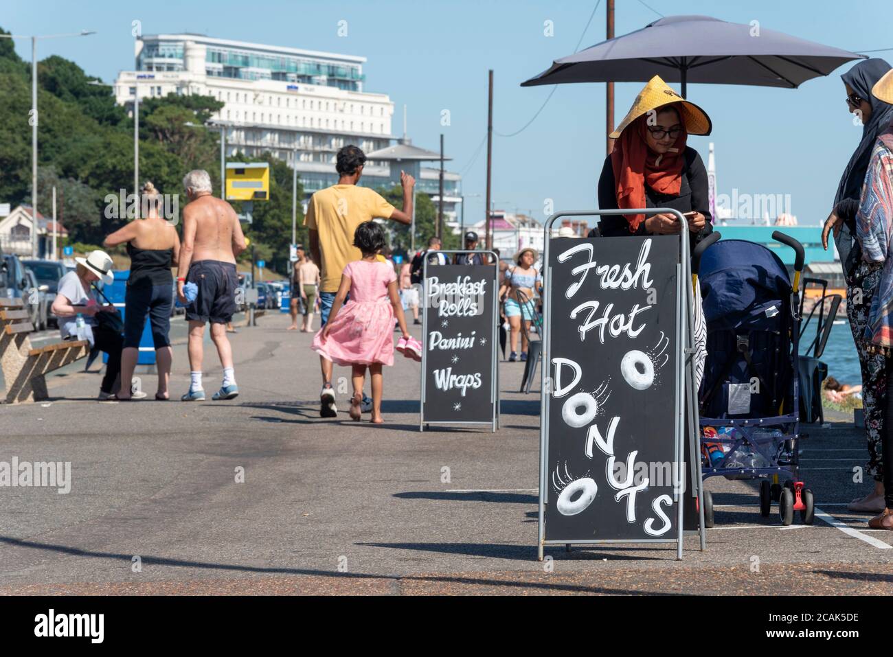 Advert for fresh hot donuts on a hot day in Southend on Sea, Essex, UK during the COVID-19 Coronavirus pandemic. Ethnic females. BAME visitors Stock Photo