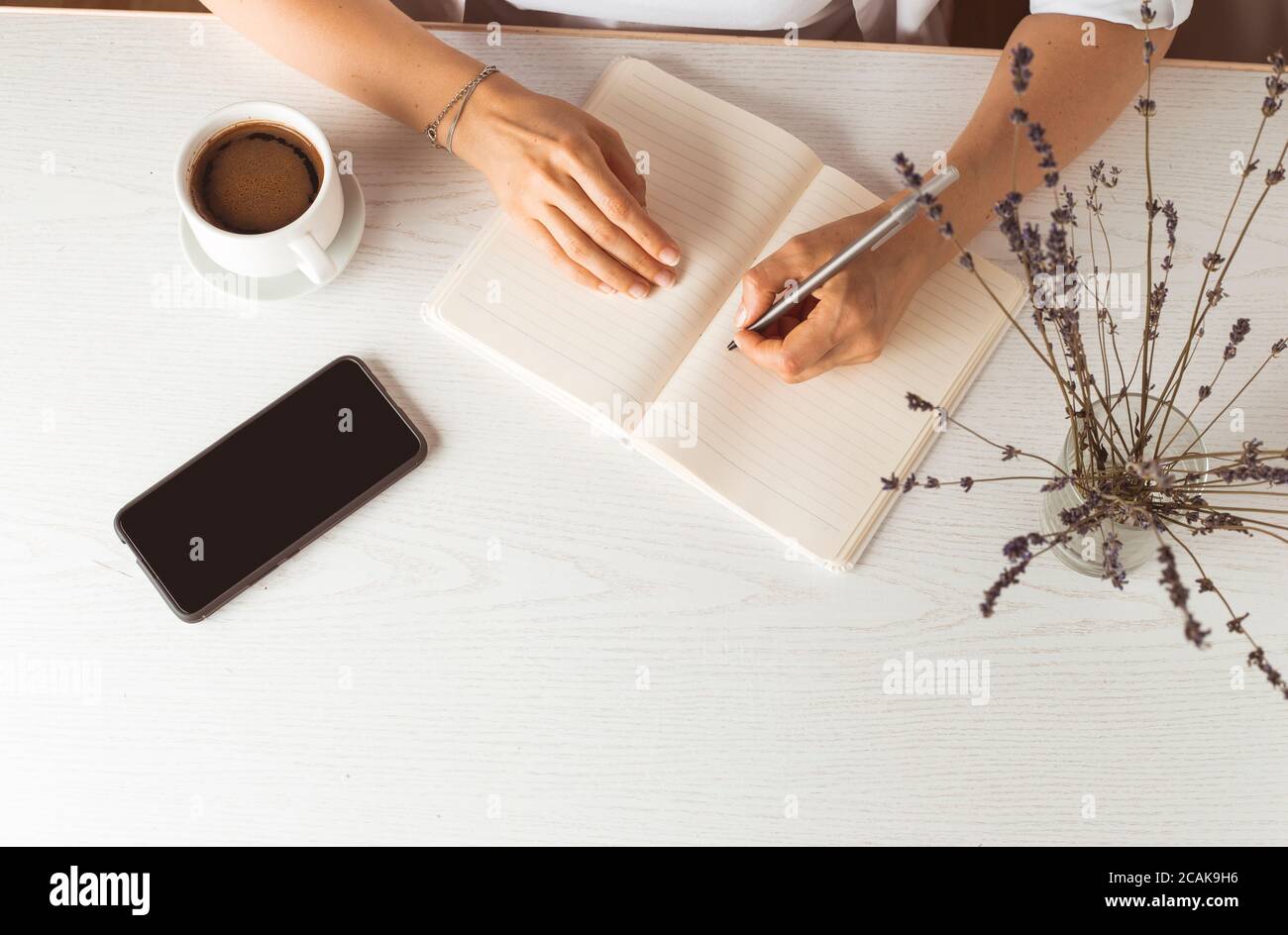A woman writes in a notebook while sitting in the room at the table. Stock Photo