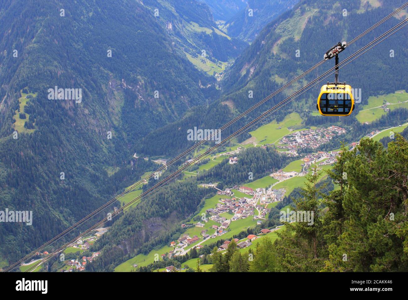 Yellow gondola cable car going down over an alpine Austrian town Mayrhofen in a mountain valley Stock Photo