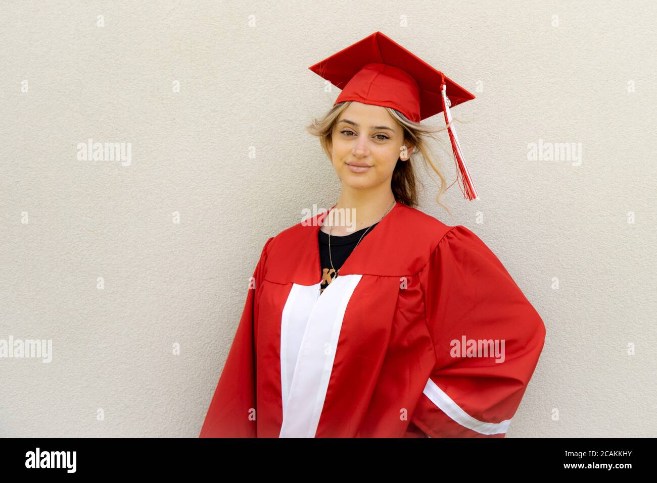 Young caucasian woman student wearing red graduation cap and gown. Stock Photo