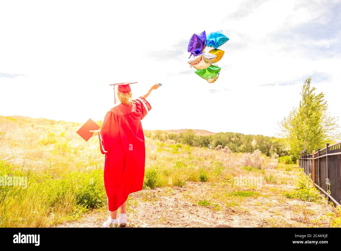 Young woman celebrating high school graduation, holding balloons and diploma. Stock Photo