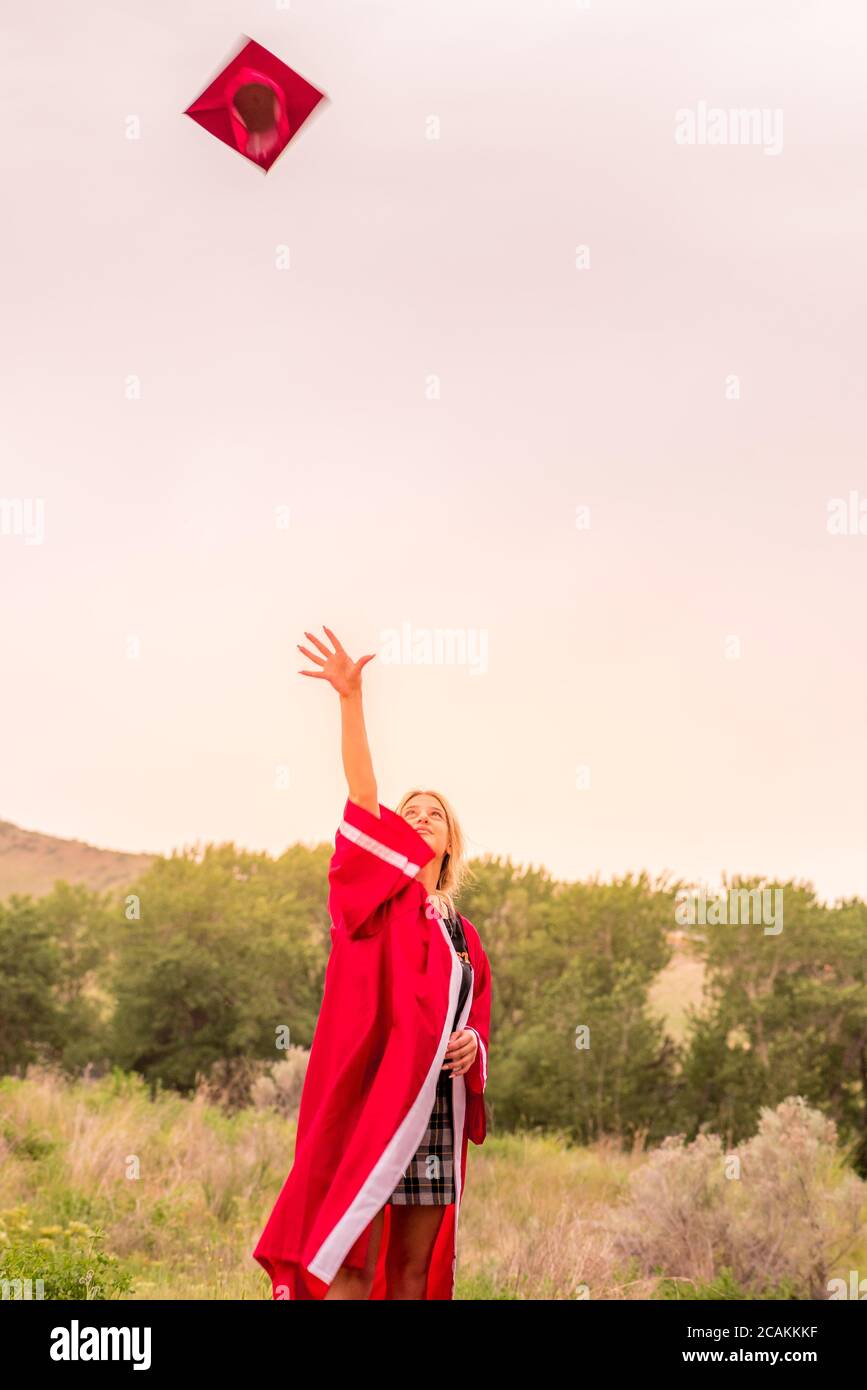 Beautiful young girl throwing red graduation cap in the air celebrating. Stock Photo