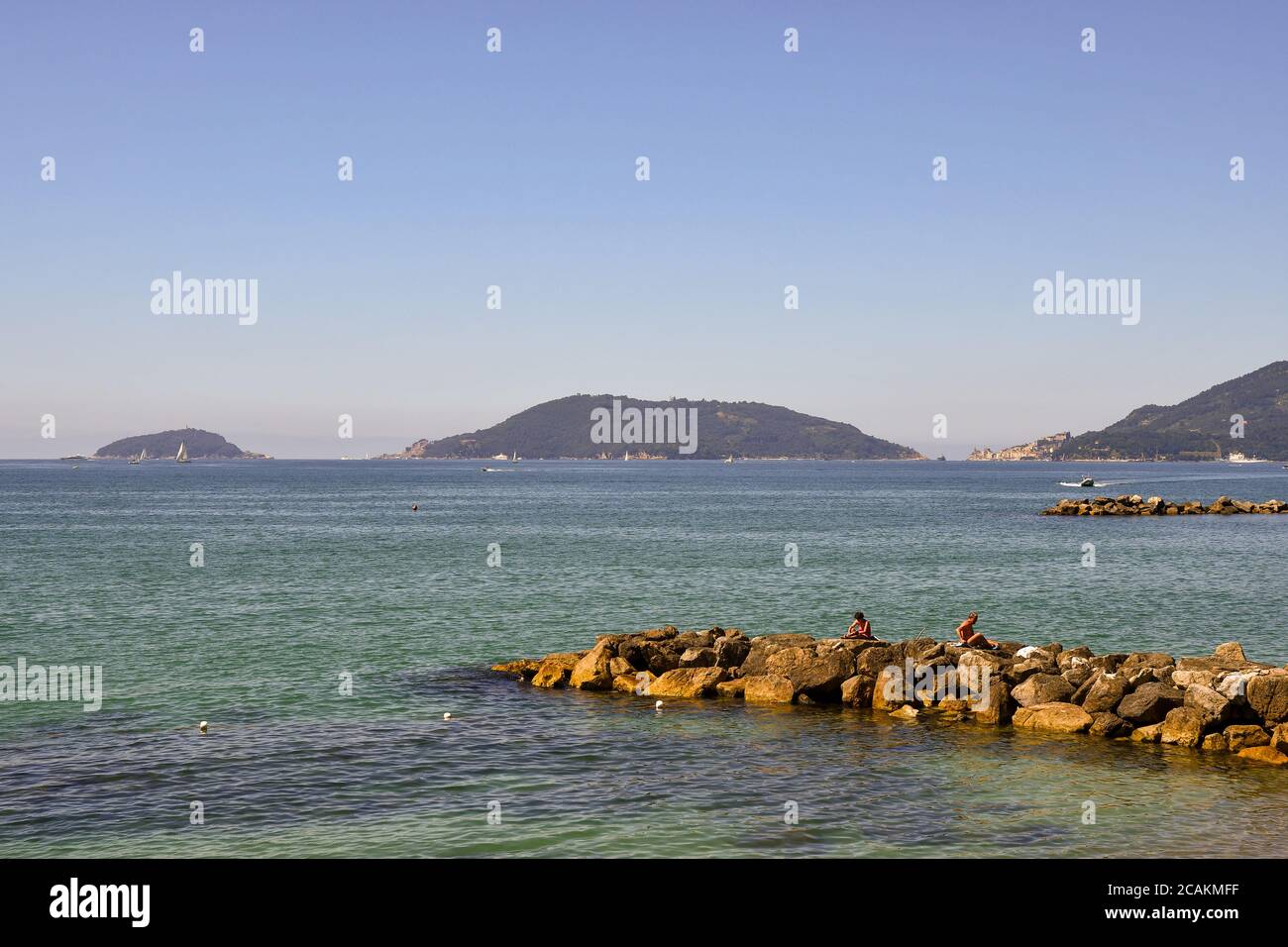 View of the Gulf of the Poets with people sunbathing on the rocks and the archipelag of Porto Venere (Unesco Site) in the background in summer, Italy Stock Photo