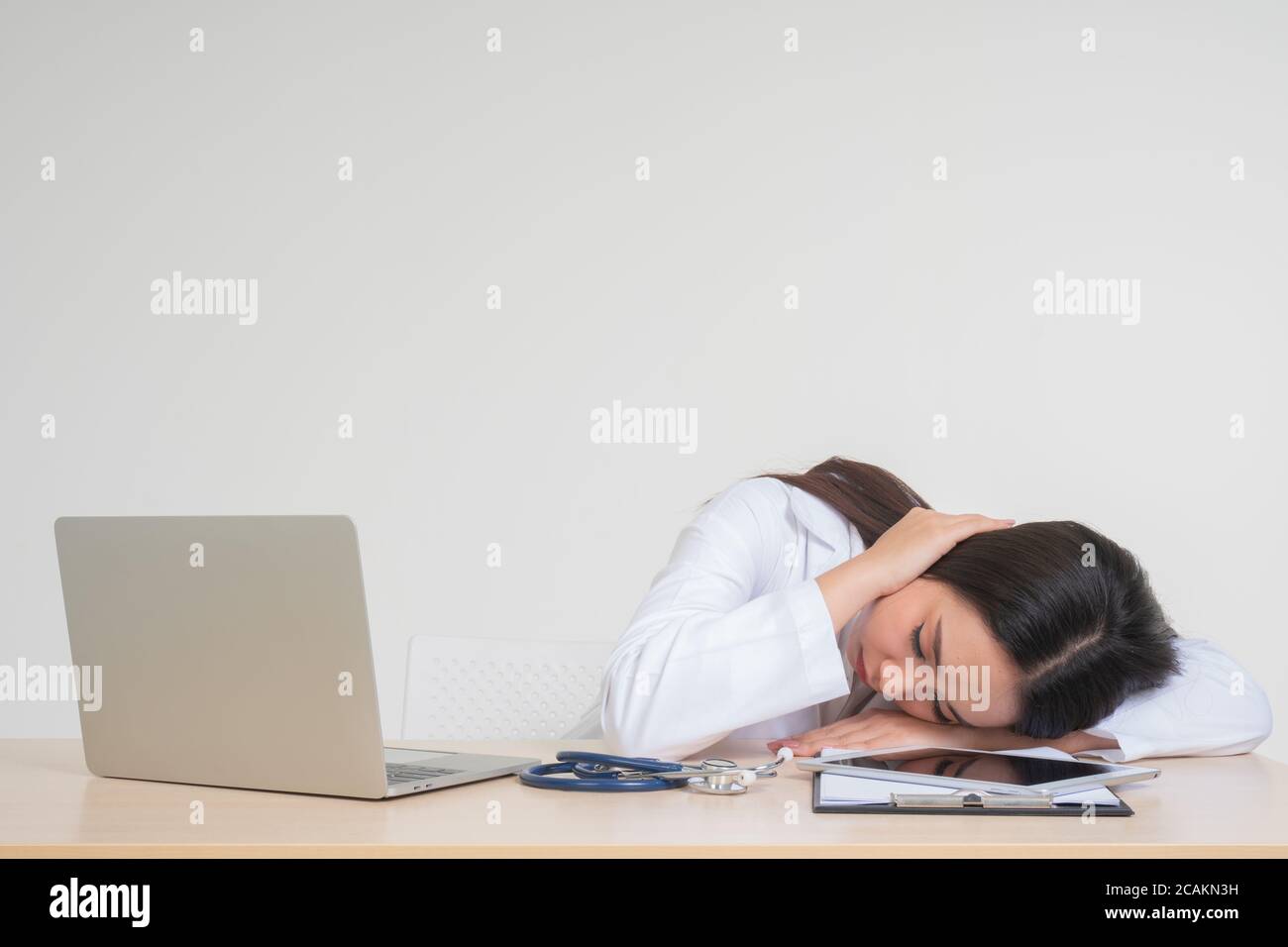 Young Asian woman doctor sitting on desk, she look unhappy and tired because of overwork, Concept of stressed exhausted and doctor liability, Dealing Stock Photo